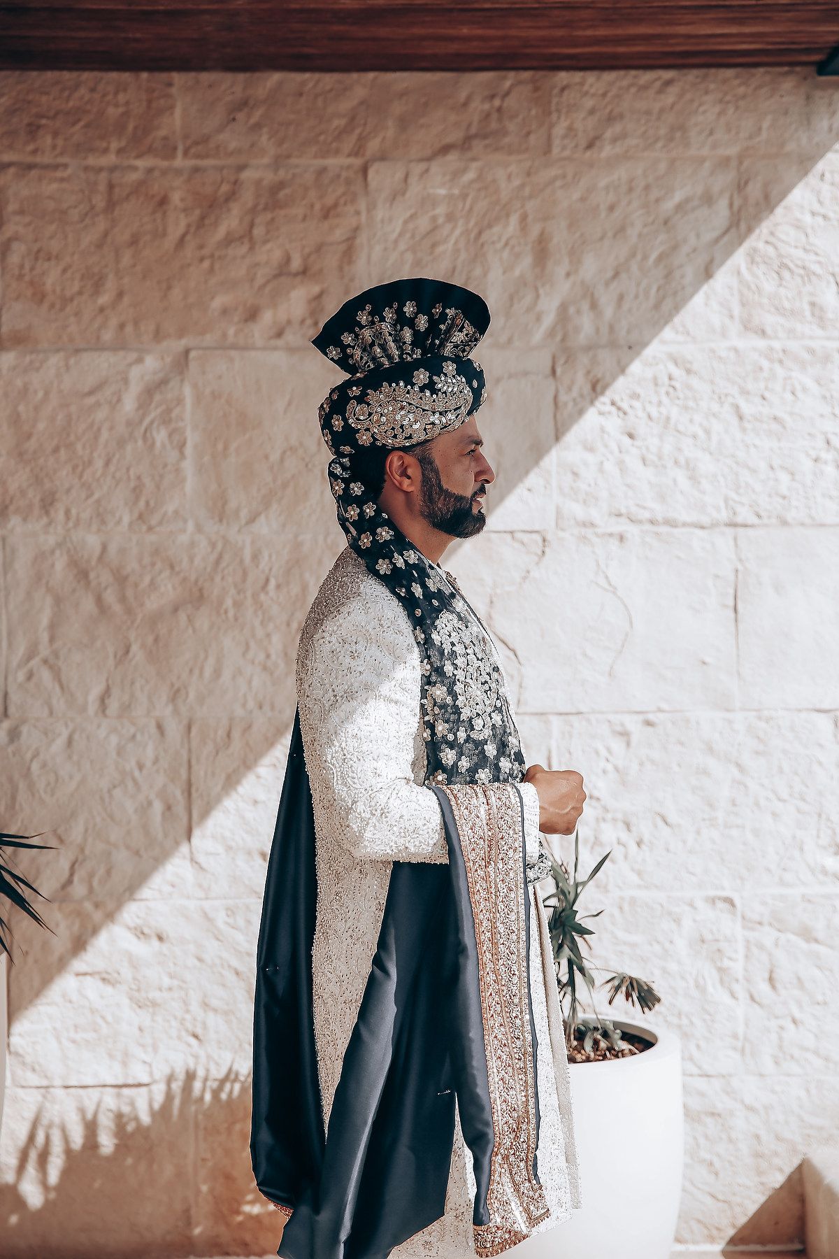 Traditional formal attire with intricate embroidery and headpiece against white wall.