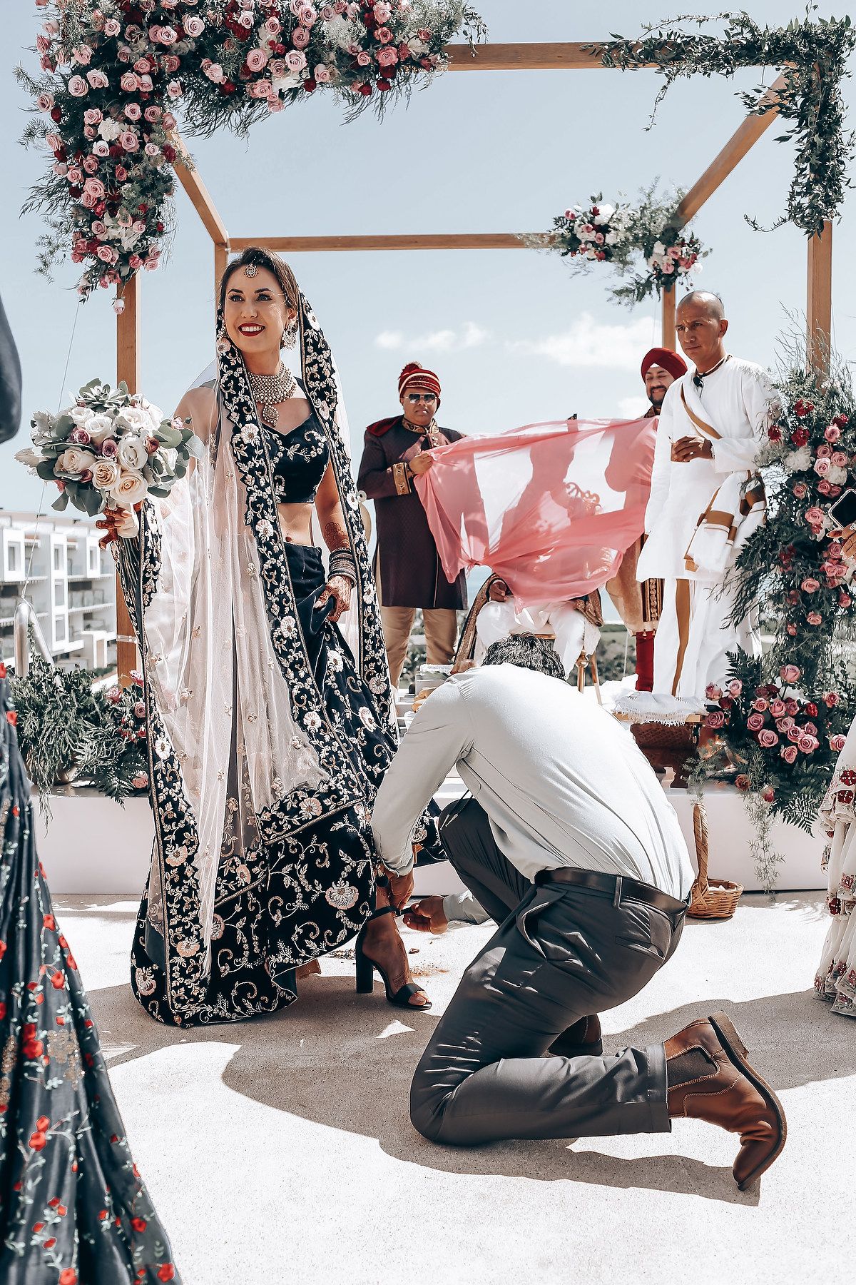 Wedding ceremony under floral arch with couple performing traditional rituals on outdoor terrace.