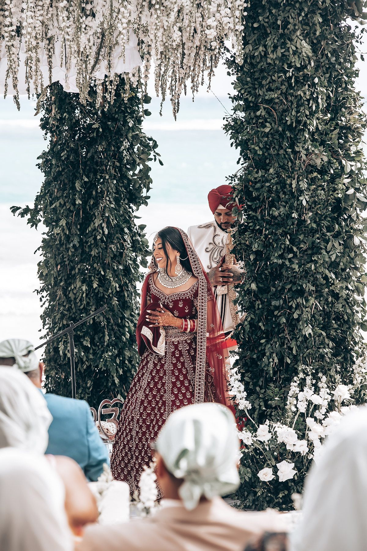 Wedding ceremony setup with hanging greenery and guests seated in white chairs.