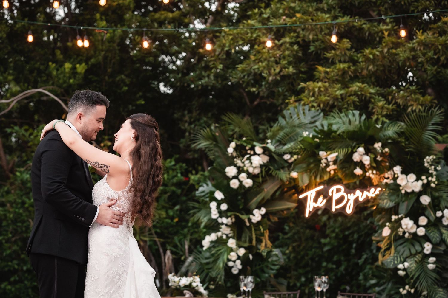 Couple shares intimate dance moves under twinkling lights and floral decorations at outdoor reception.