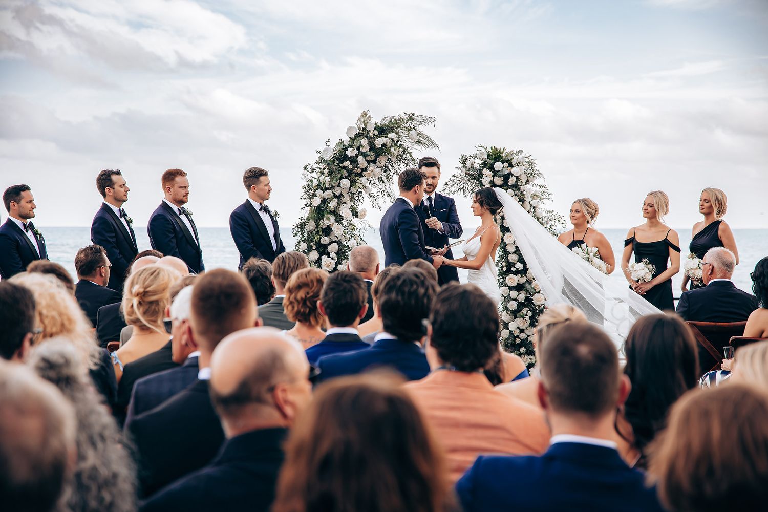 Outdoor wedding ceremony with floral arch and seated guests overlooking scenic view.