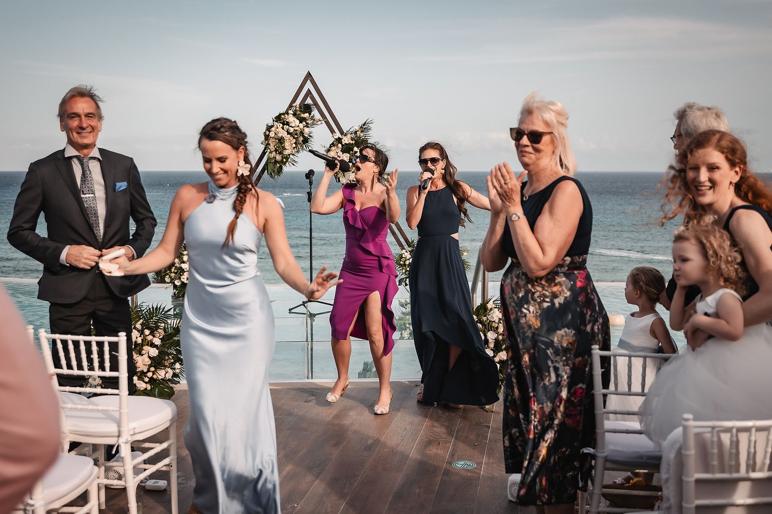 Guests mingle and socialize at an elegant beachfront wedding reception with white chairs.