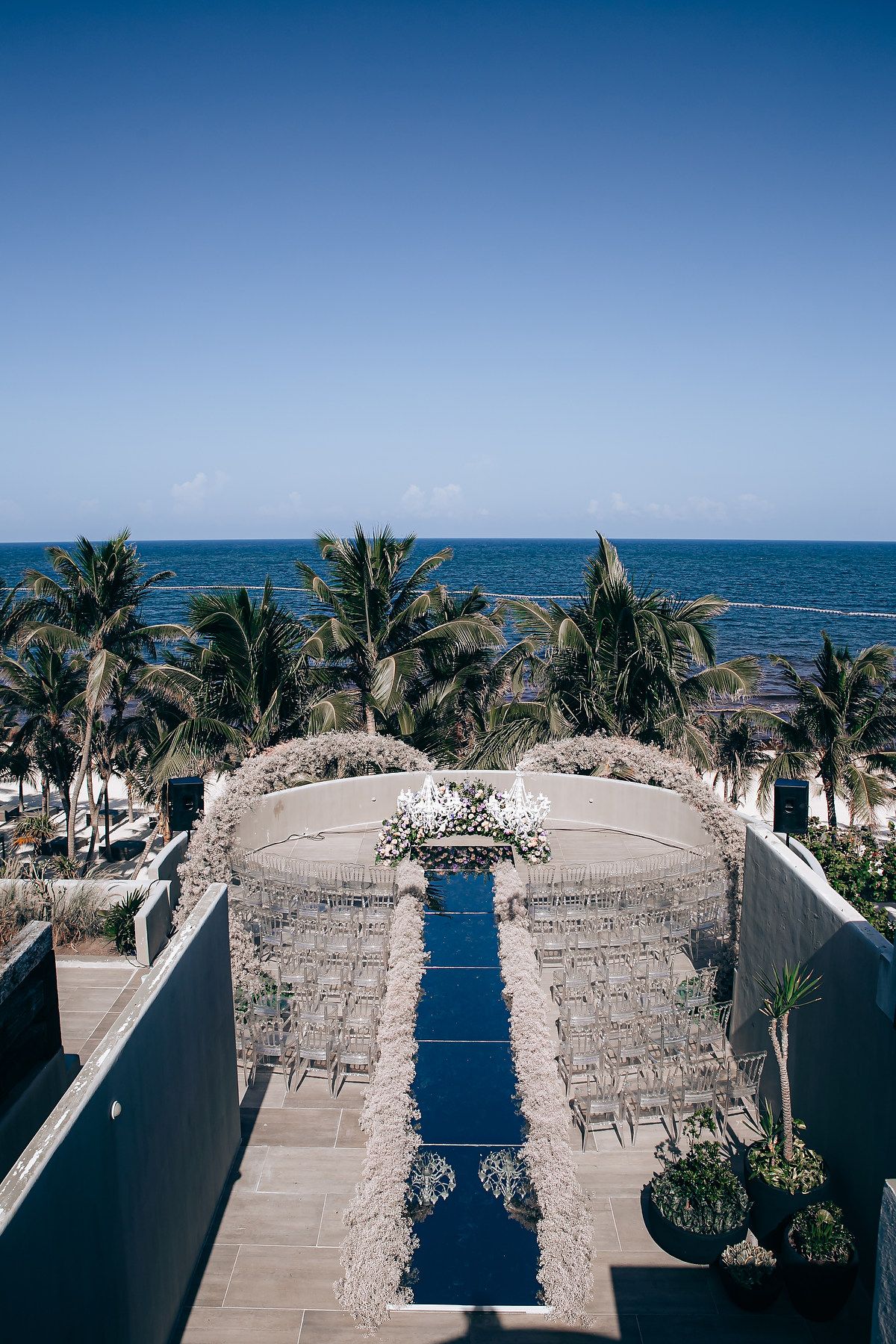 Aerial view of a beachfront wedding venue with white chairs arranged in rows under blue skies.
