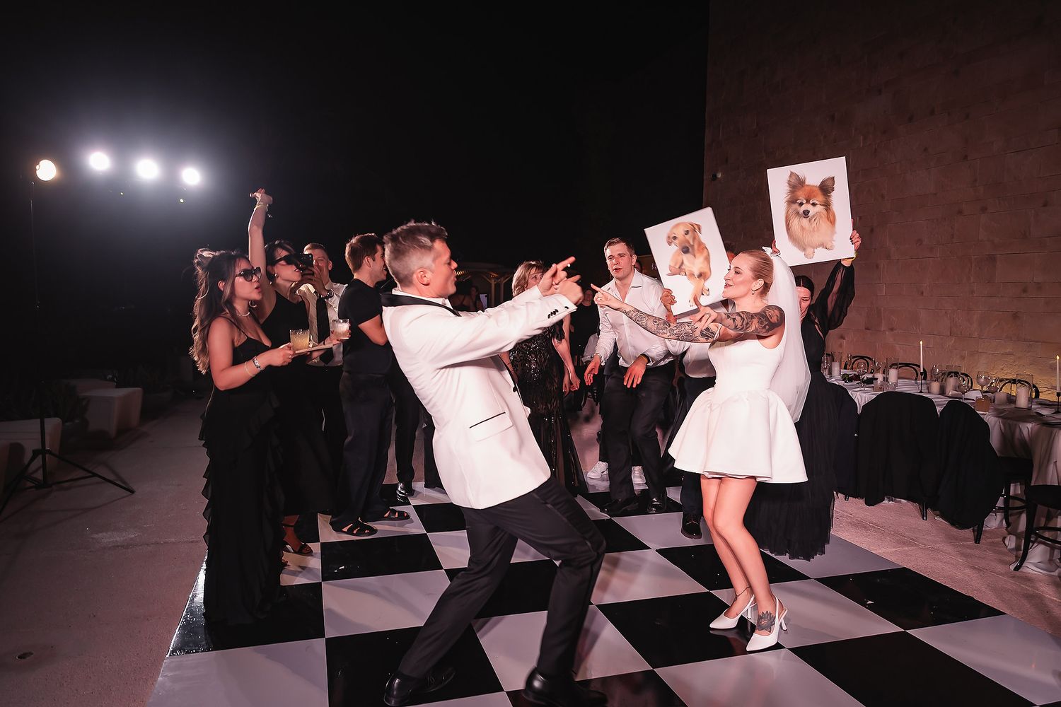Lively reception celebration on black and white checkered dance floor with party lighting.