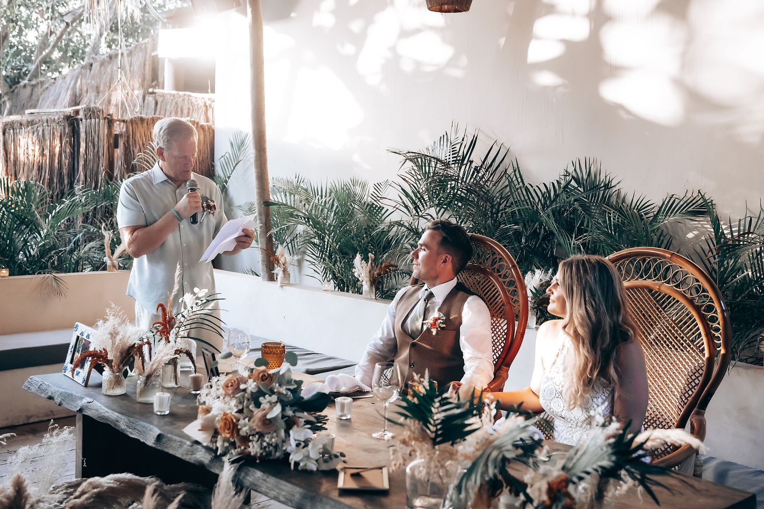 Friends enjoying drinks and conversation at a tropical-themed restaurant with palm trees and natural lighting.