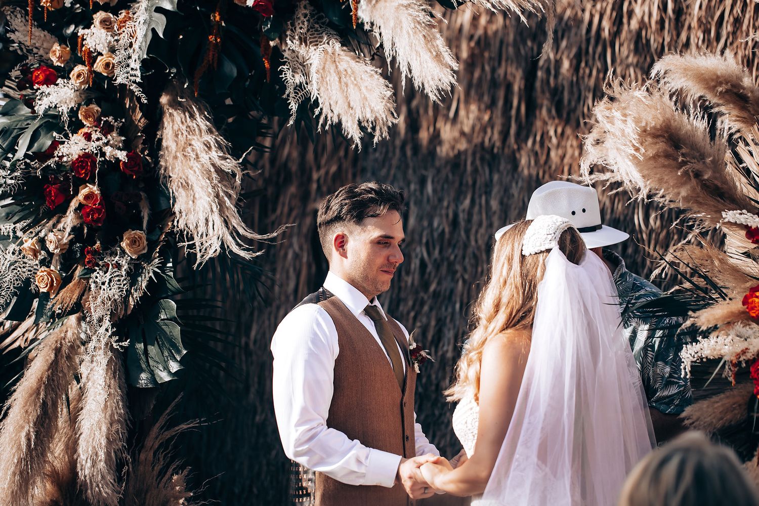 Wedding ceremony scene under rustic pampas grass and dried palm decor at an outdoor venue.