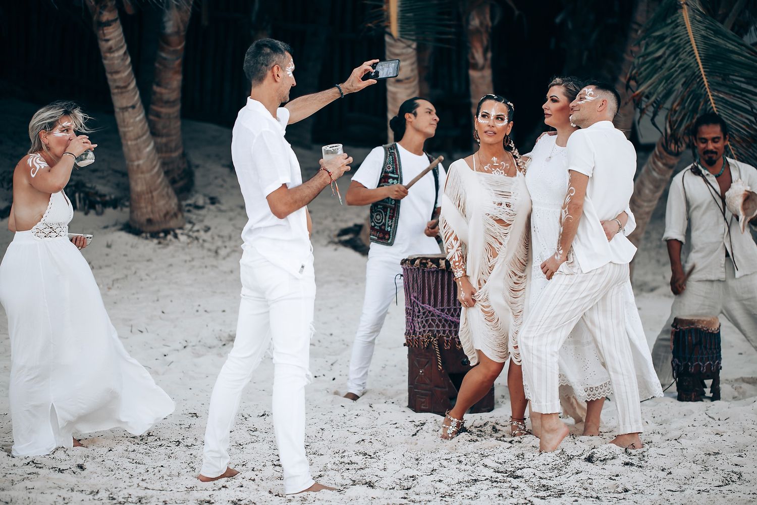 A group celebrating on the beach in coordinated white outfits.