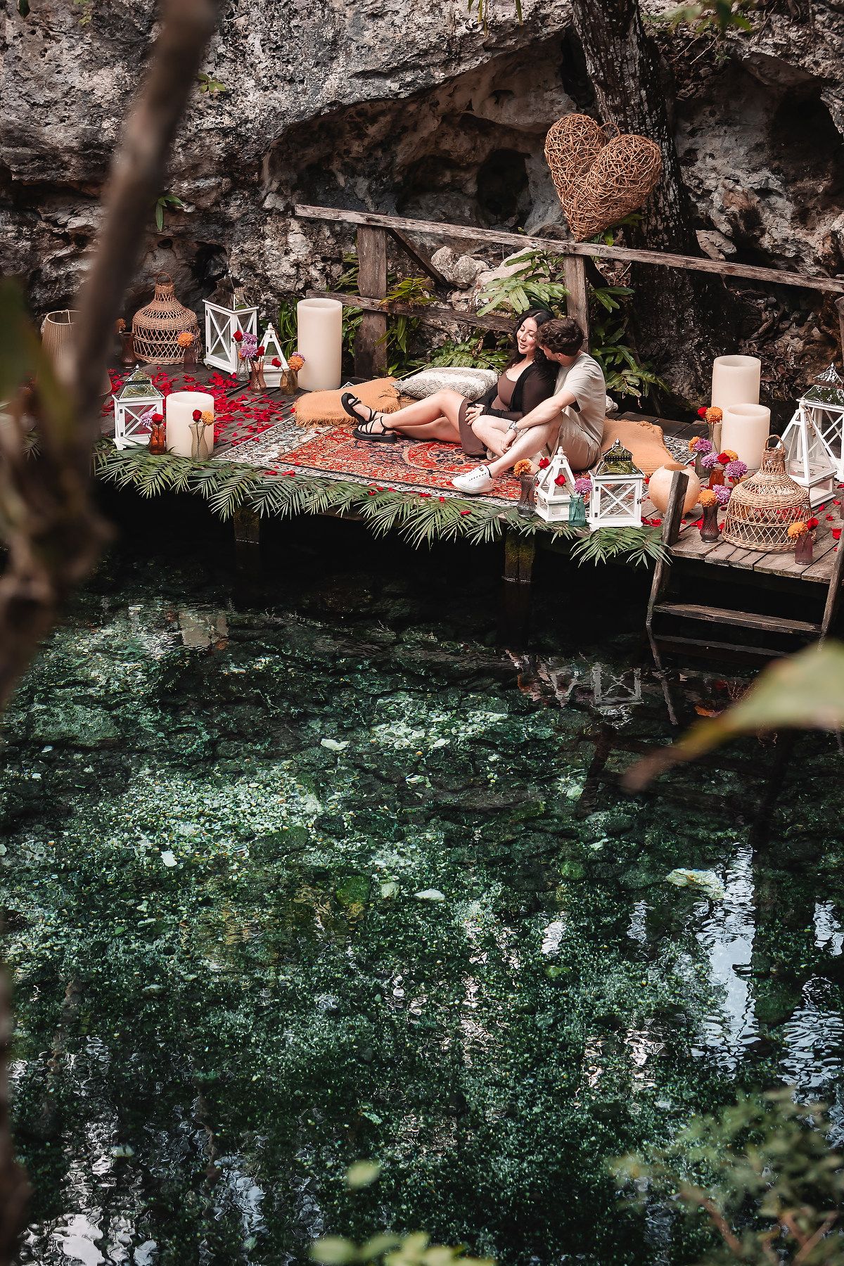 Scenic view of a natural cenote pool with decorative elements and lounging area along rocky edge.