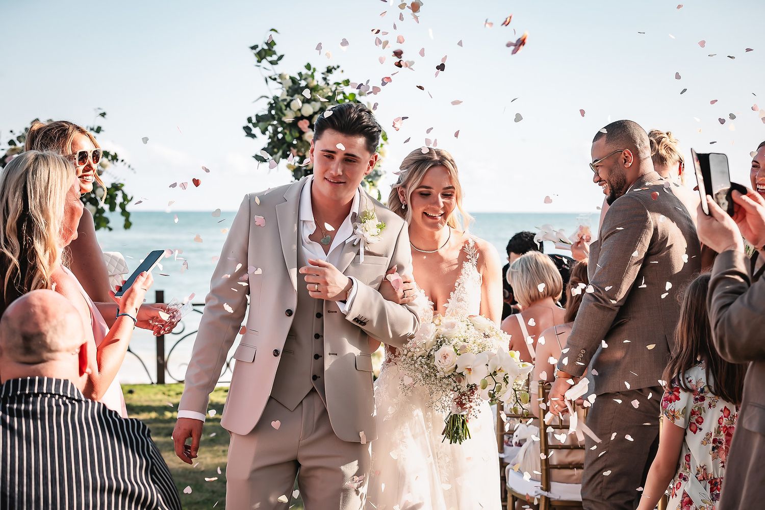 Wedding party throws colorful flower petals during an outdoor celebration by the ocean.