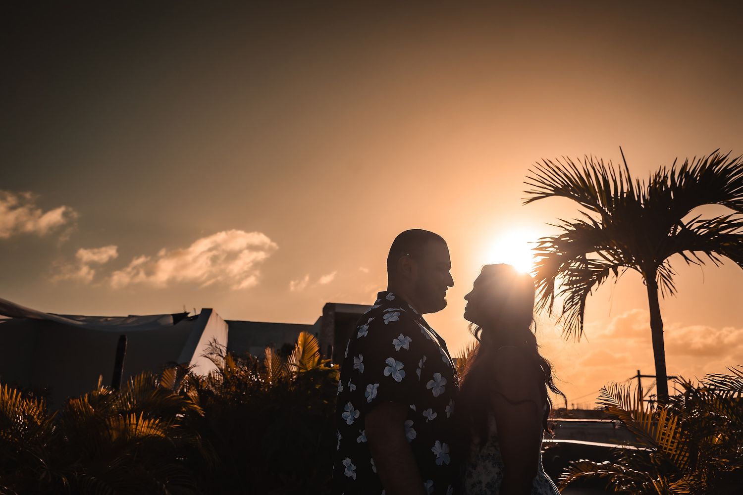 Silhouette of palm trees and buildings against a dramatic sunset sky.
