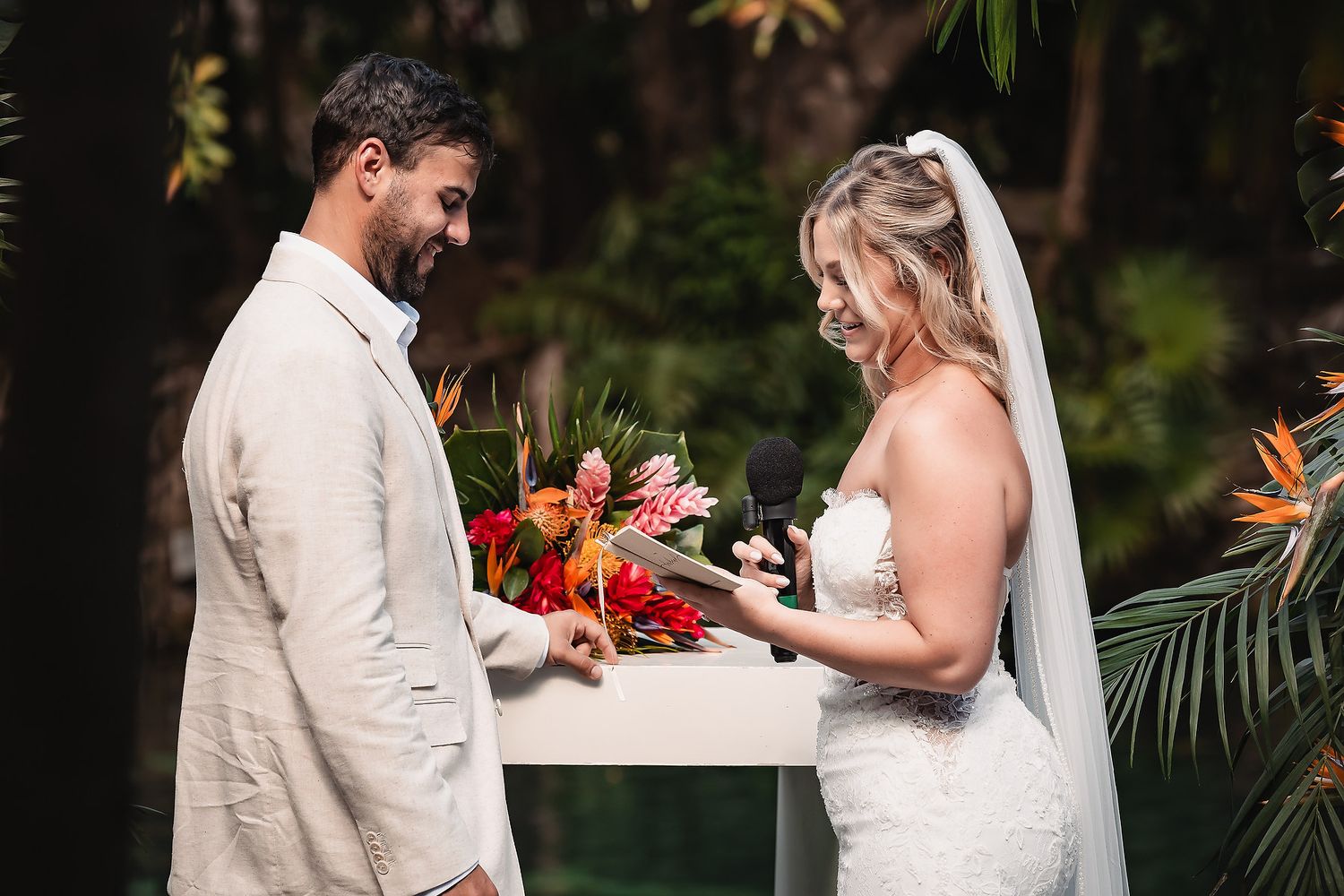 Intimate wedding ceremony moment under a tropical floral arrangement with red blooms.