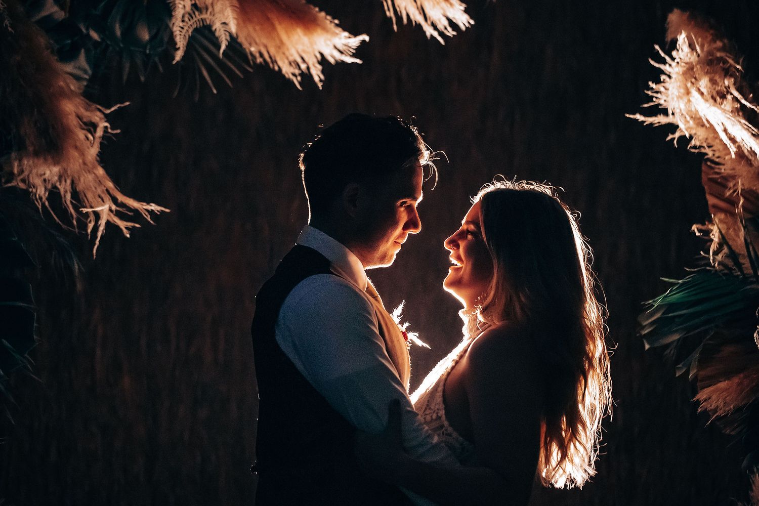 Romantic beach wedding couple dancing at sunset with palm trees silhouetted in the background.