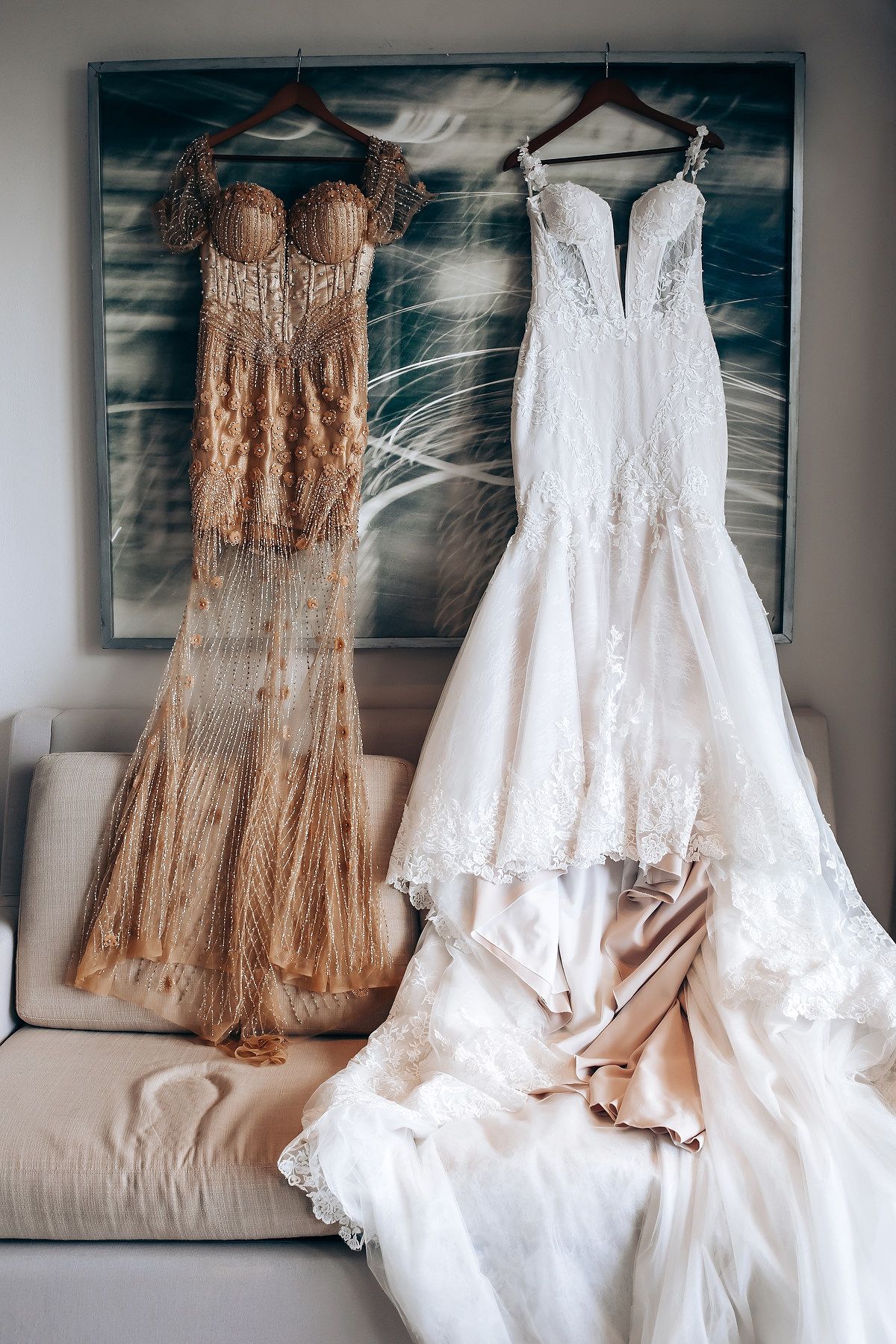Wedding dresses and bridesmaid gowns in blush tones hanging on display against a gray wall.