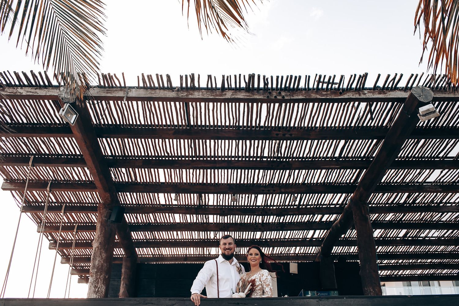 Couple walking under a palm-frond covered pergola at a tropical resort destination.