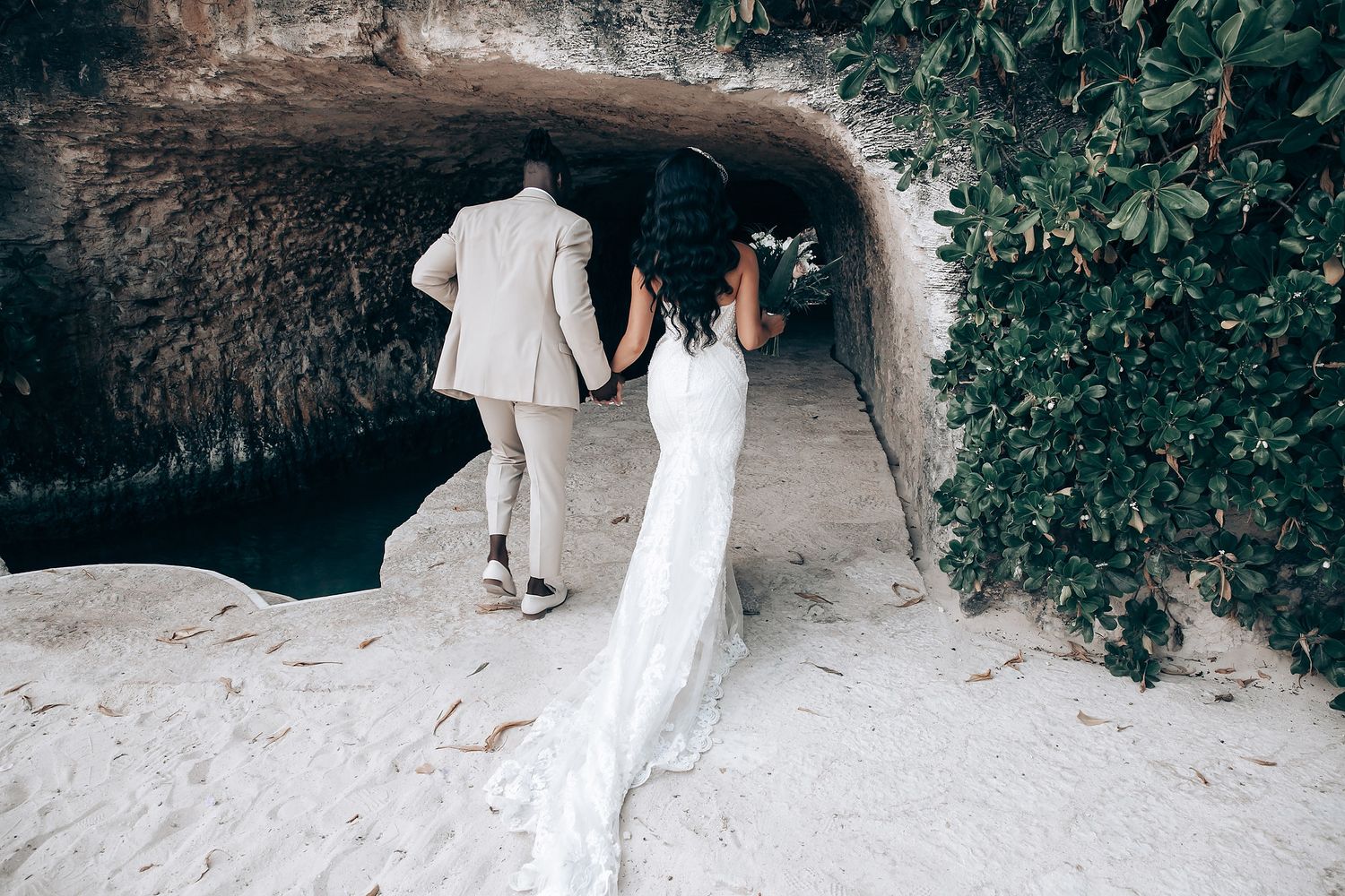 Romantic couple embraces in a stone archway surrounded by lush greenery during outdoor wedding photoshoot.