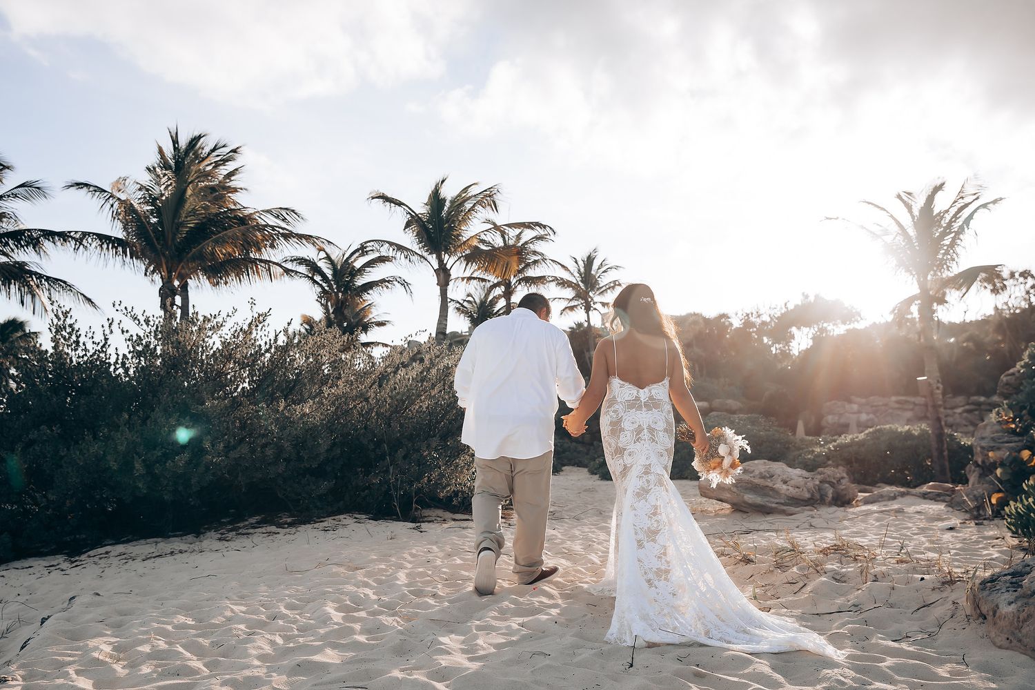 Sunset beach wedding photography session with palm trees silhouetted against cloudy sky.