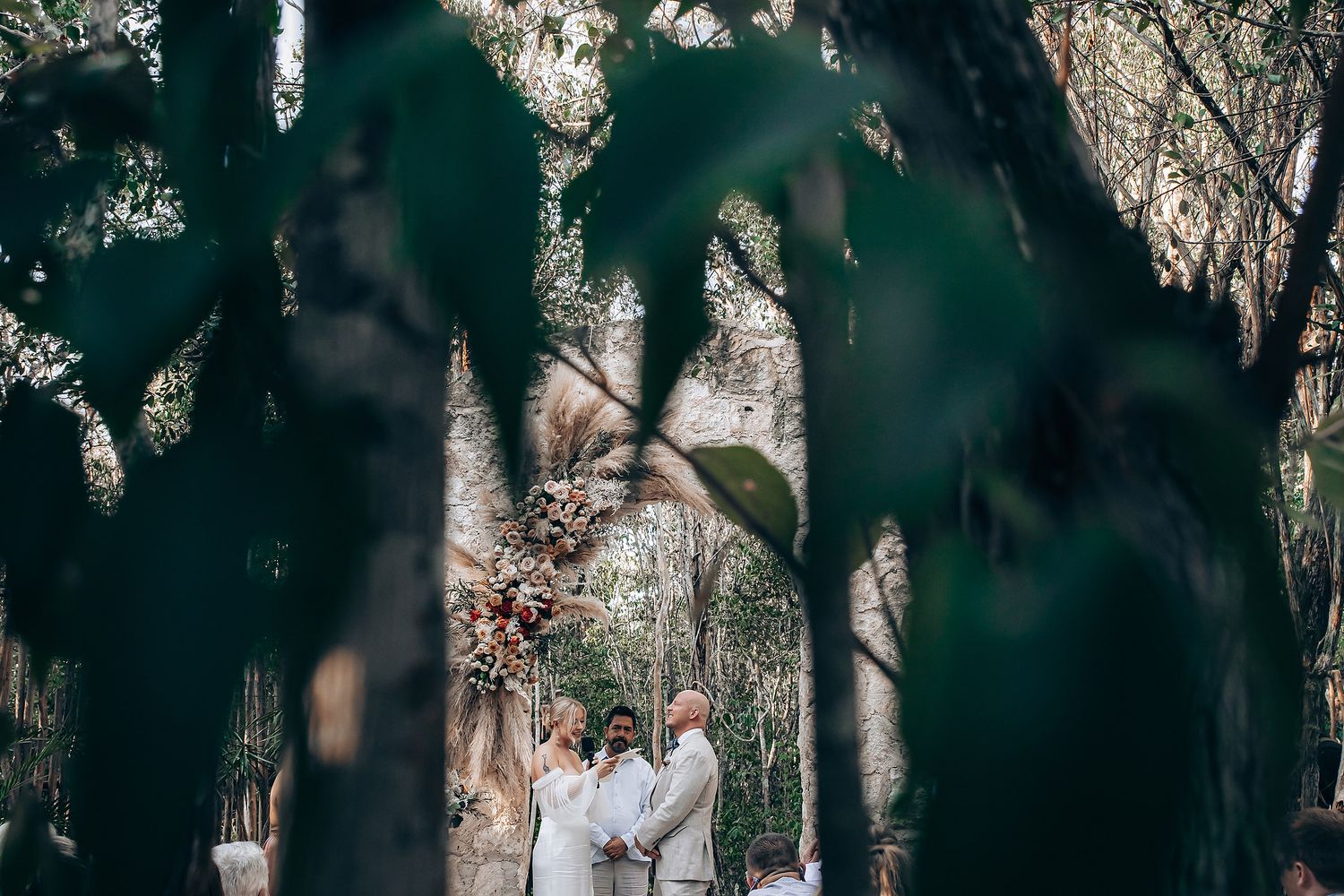 A couple shares an intimate moment in a wooded outdoor setting surrounded by trees and natural light.