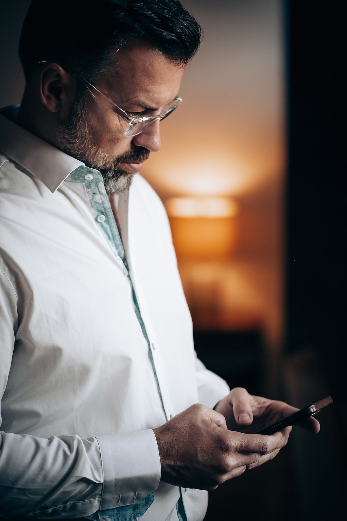 Person in white shirt looking at mobile phone screen with dramatic sunset lighting in background.