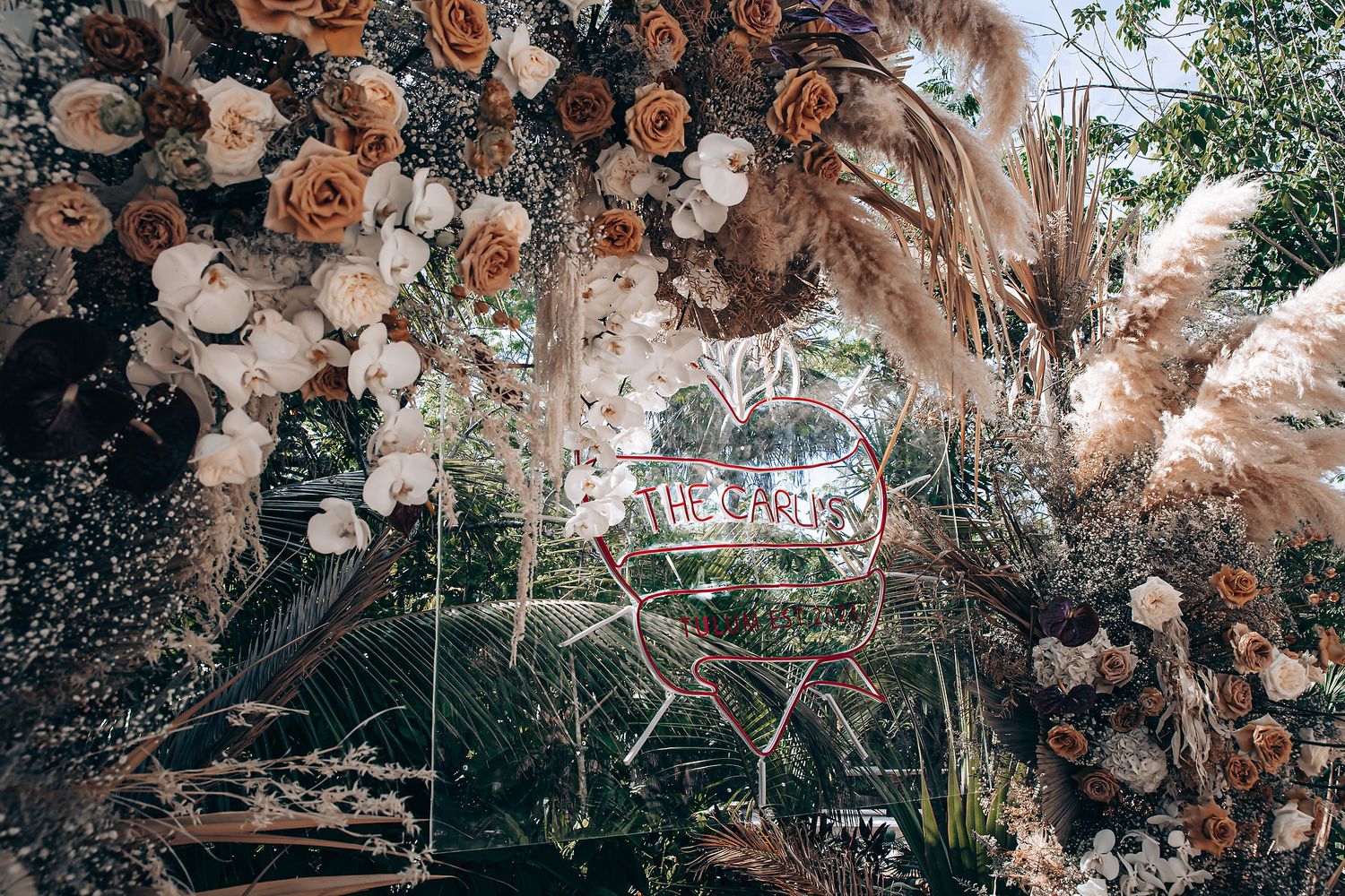 A rustic outdoor wedding arch decorated with peach and white flowers against a natural garden backdrop.