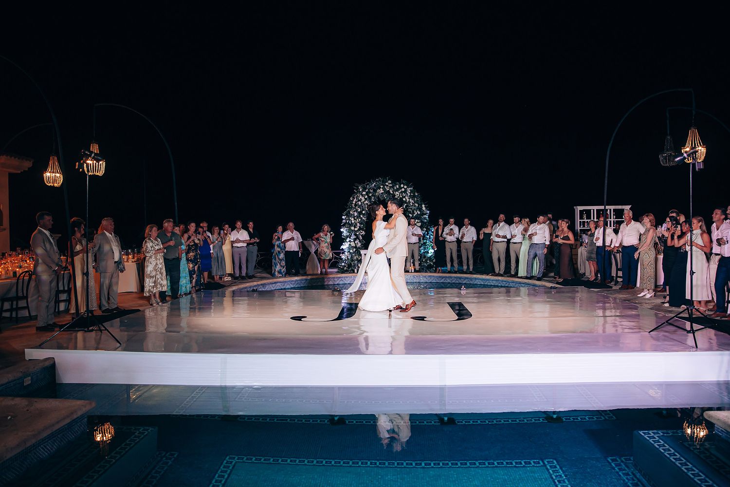 White dance floor surrounded by guests at an elegant outdoor nighttime wedding reception.