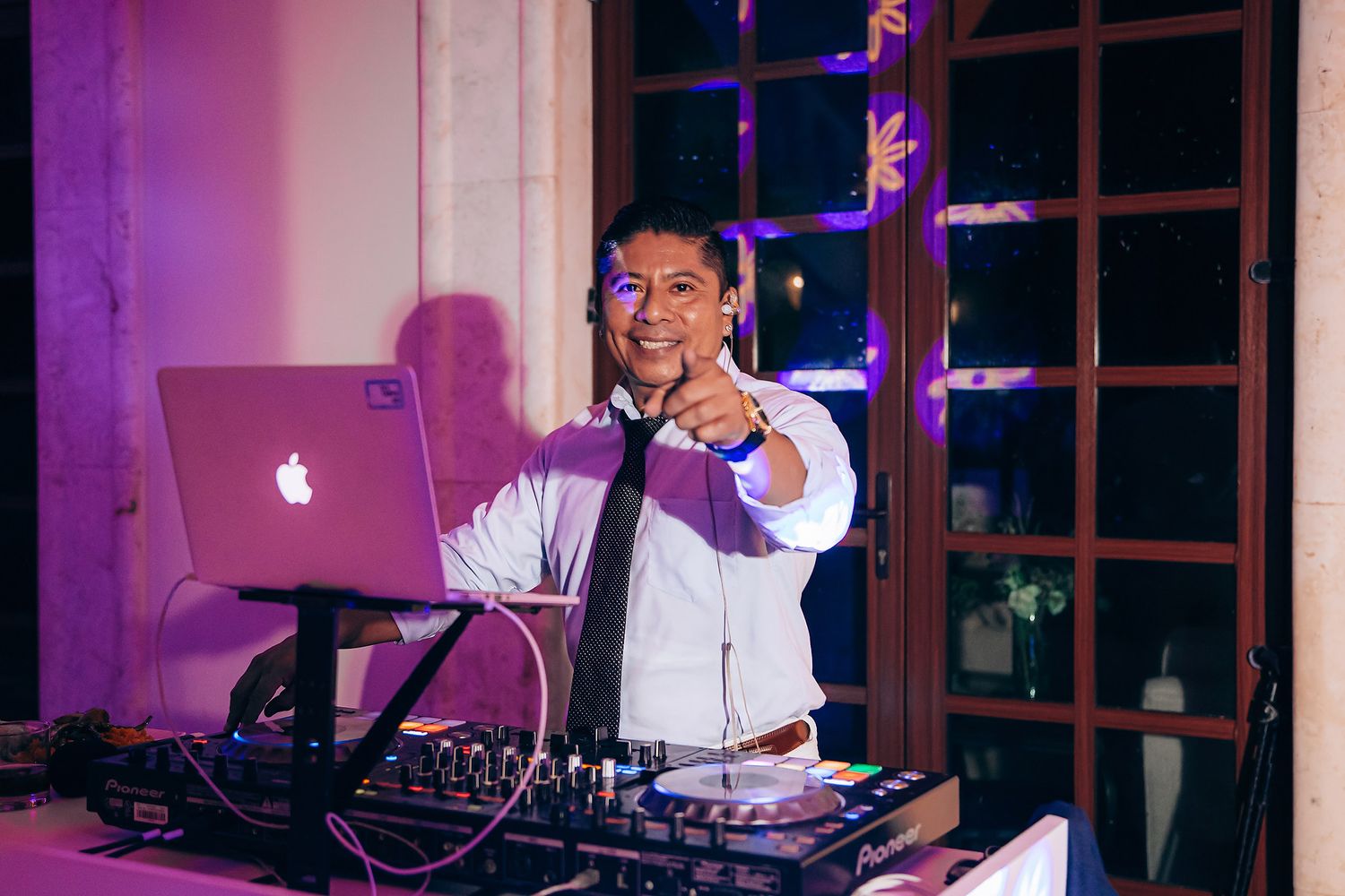 A DJ performs at a wedding reception with purple ambient lighting and equipment setup.