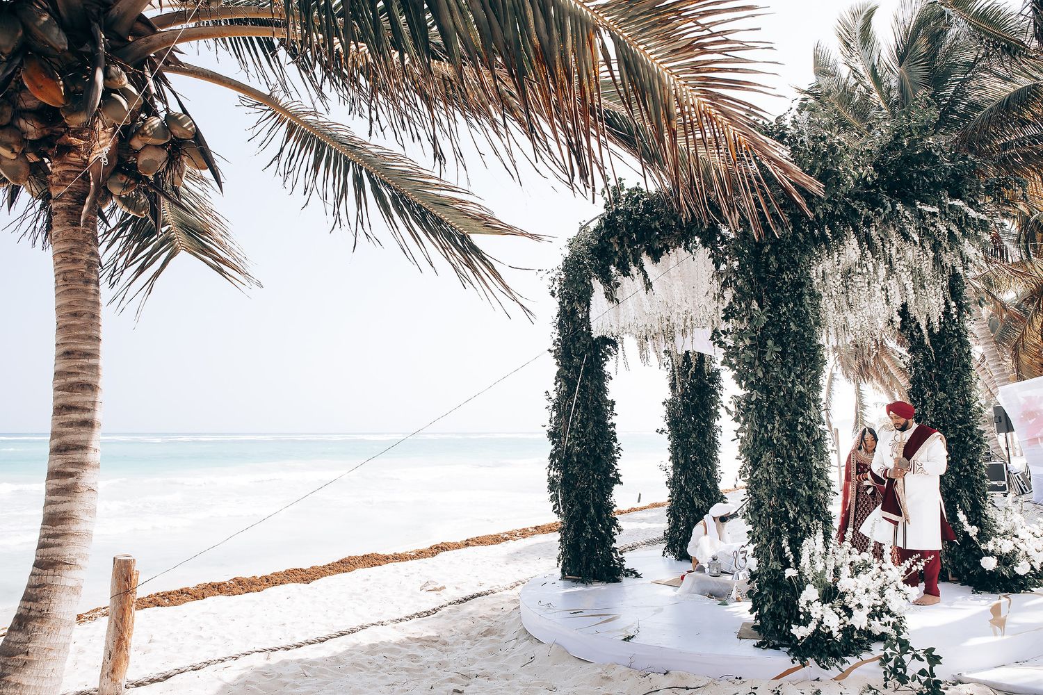 Beachfront wedding venue with palm trees and white decorations along the shoreline.