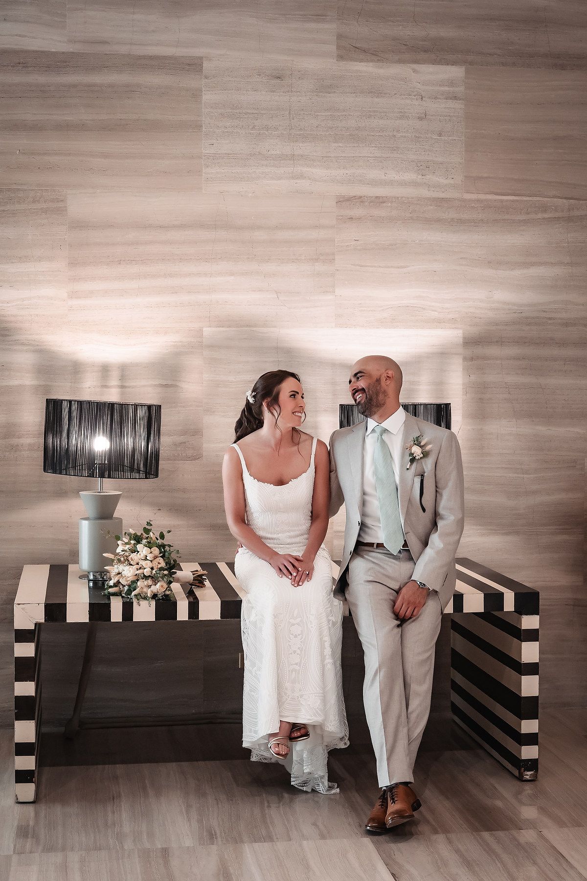 A couple in wedding attire shares intimate moments against a modern wood-paneled wall with black art pieces.
