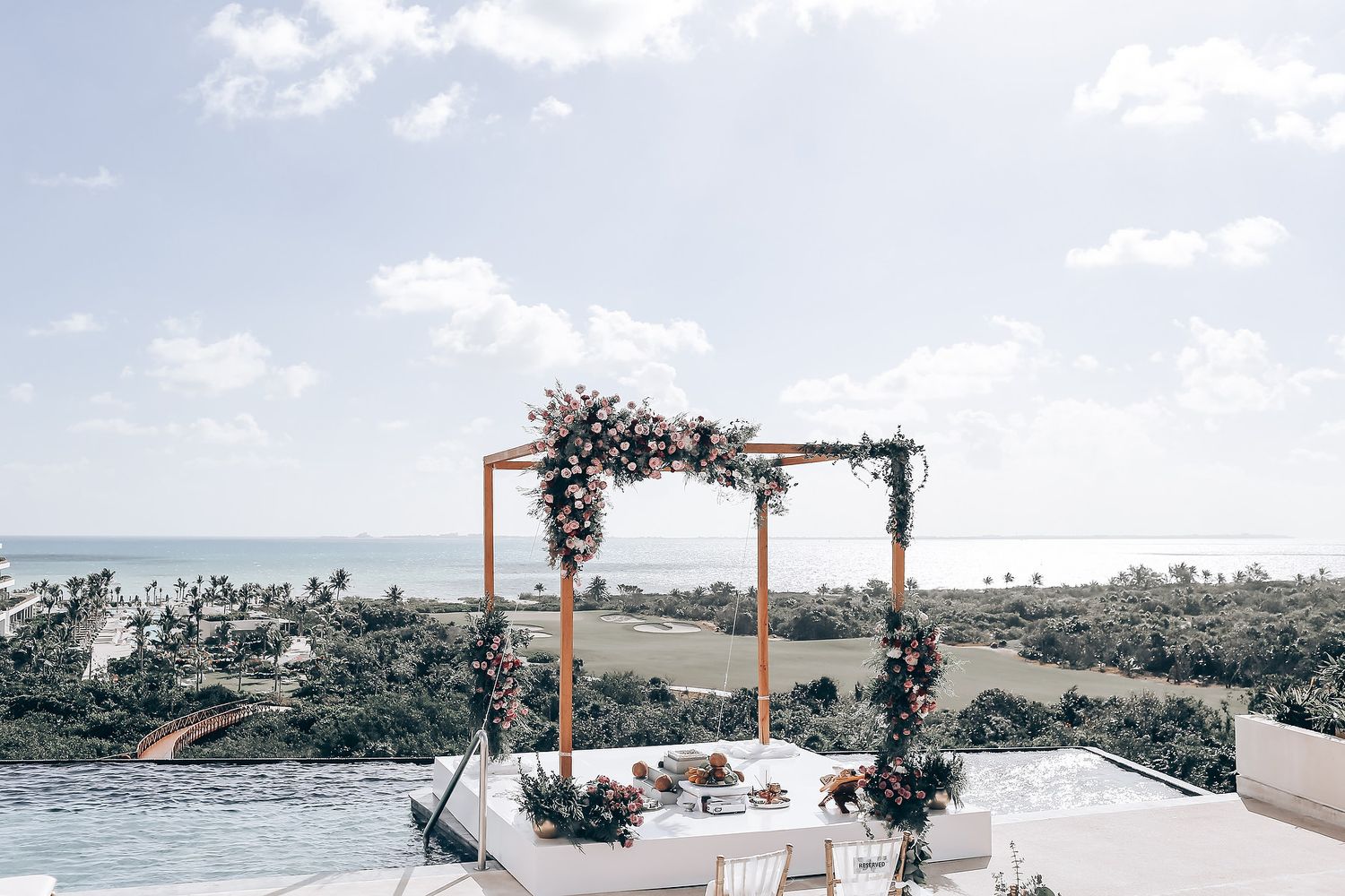 Elegant outdoor wedding ceremony setup with white floral arrangements and ocean view backdrop.