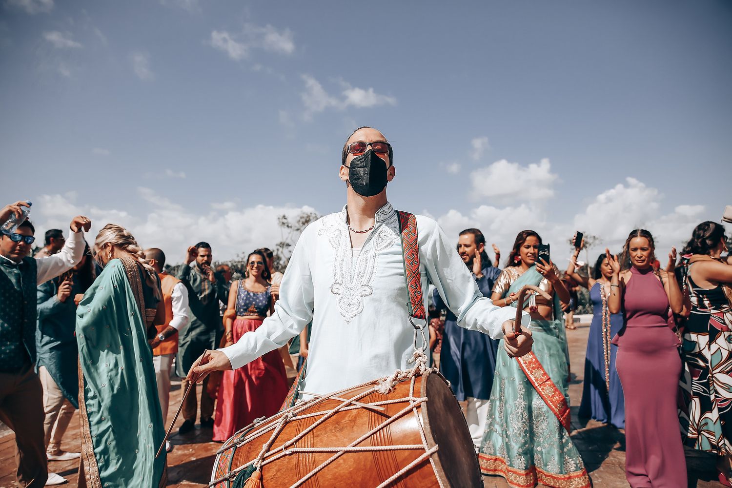 Outdoor celebration scene with guests in colorful traditional attire gathering under blue skies.
