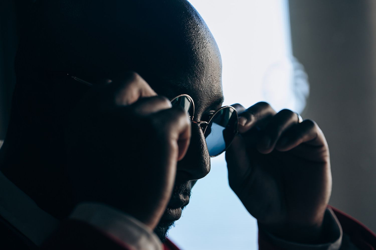 Silhouetted profile view of person adjusting sunglasses against bright backlight.