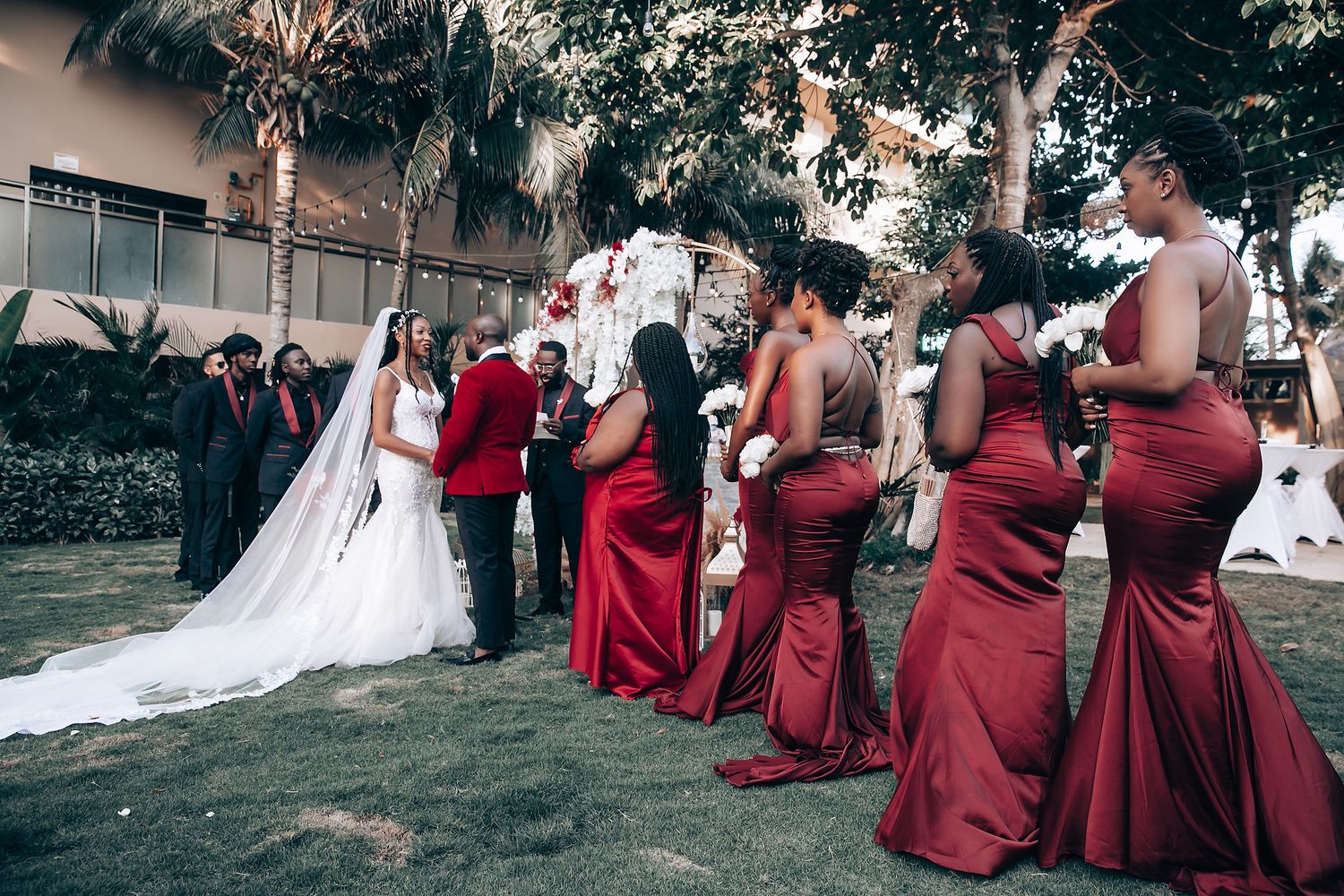 Wedding party gathered outdoors with bridesmaids in deep red dresses.
