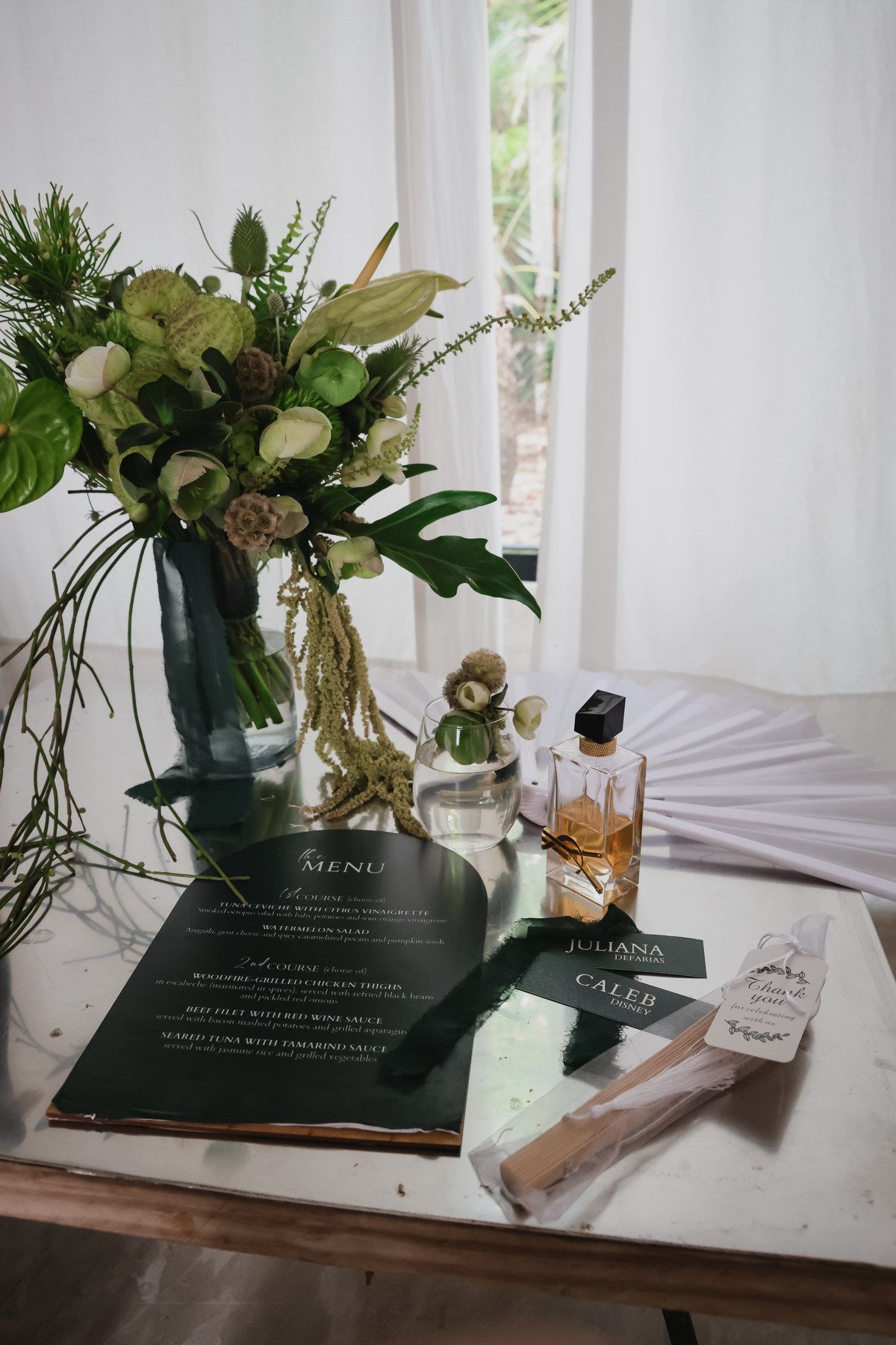 Wedding reception table with floral arrangement, menu cards, and perfume bottle centerpiece.