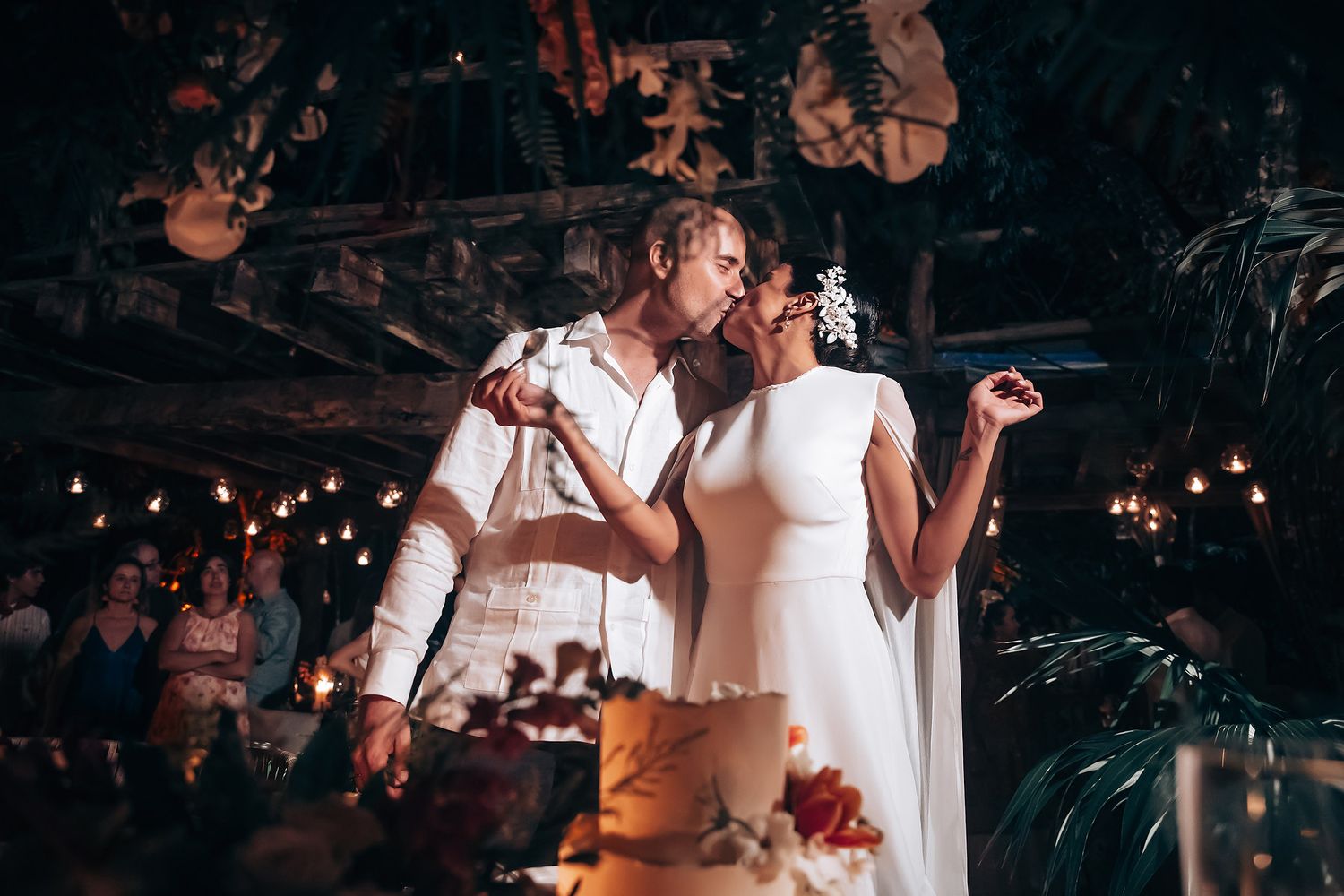 A couple shares an intimate moment while cutting their wedding cake at a rustic reception venue.