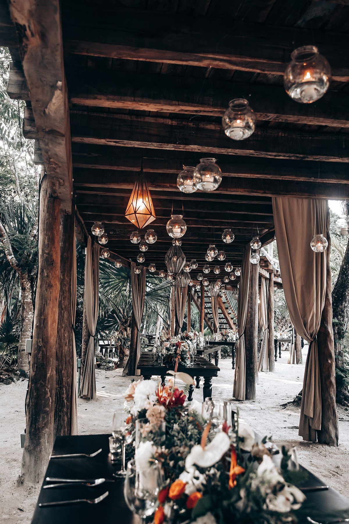 Rustic outdoor wedding venue with wooden beams and hanging glass lanterns creating a romantic atmosphere.