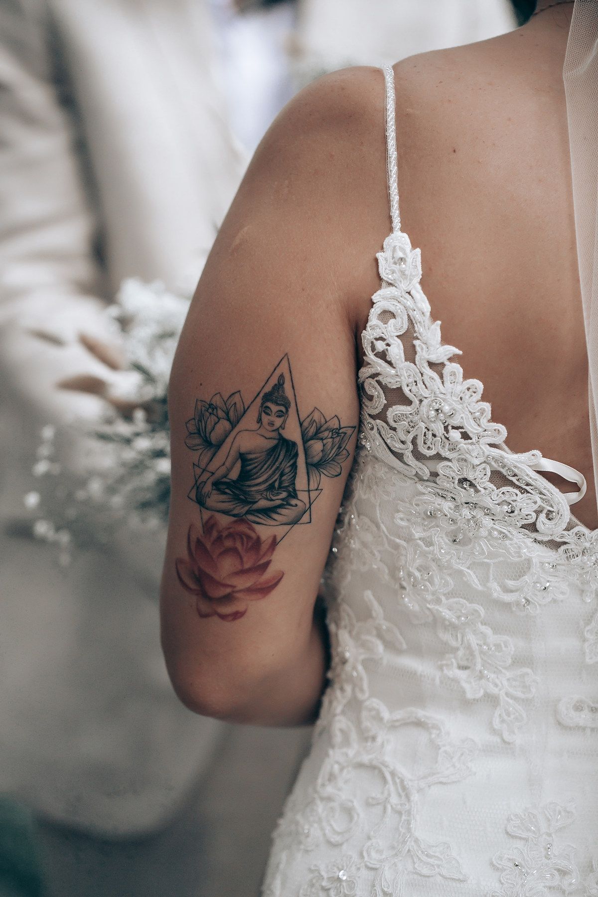 Close-up detail of a delicate lace wedding dress contrasting with a dark tattoo on the arm.