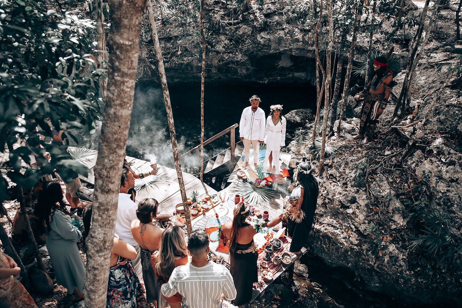 A romantic outdoor wedding ceremony in a wooded setting with guests seated among trees.