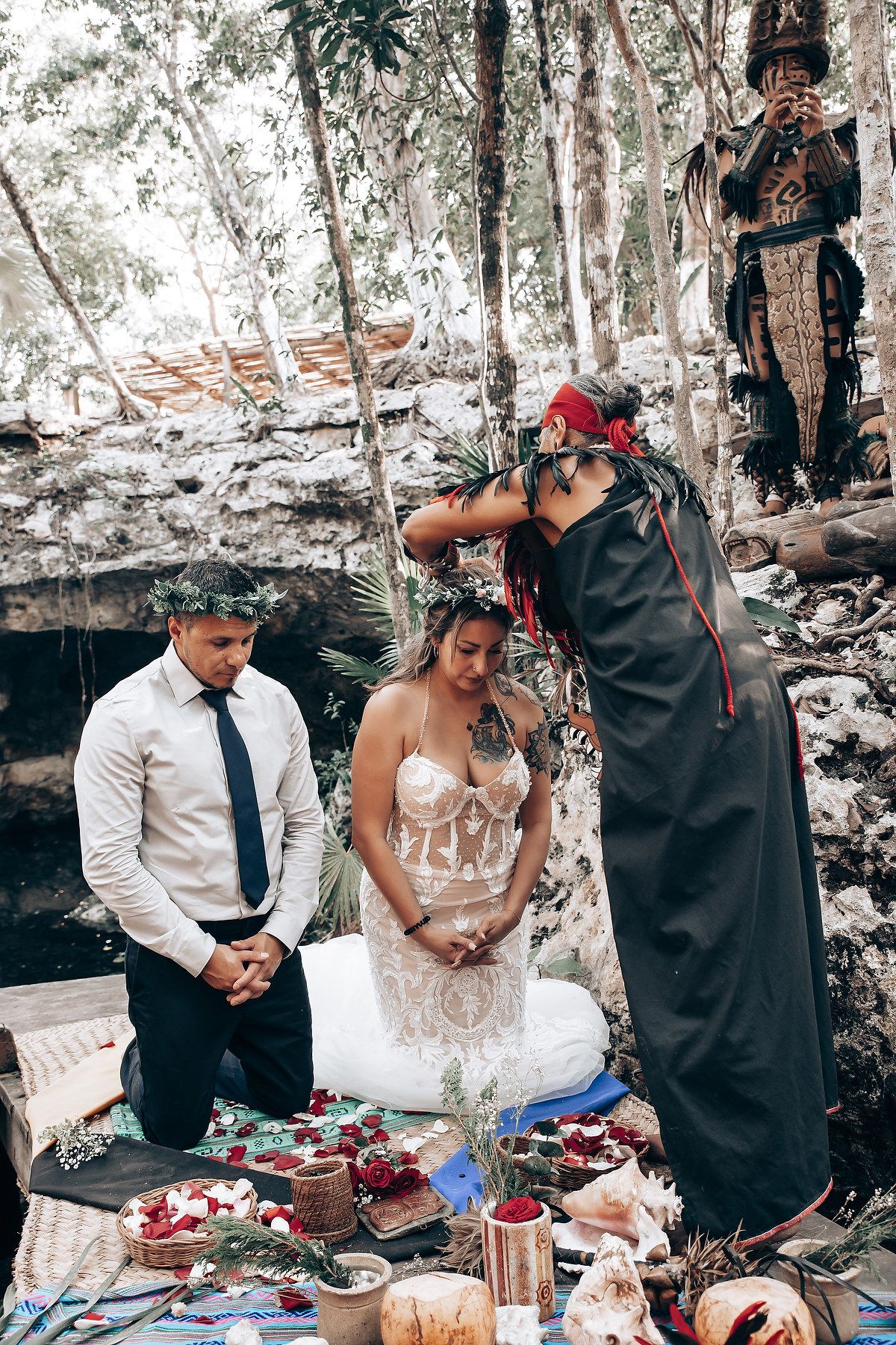 An intimate outdoor wedding ceremony features a decorated table with ritual items in a natural setting.