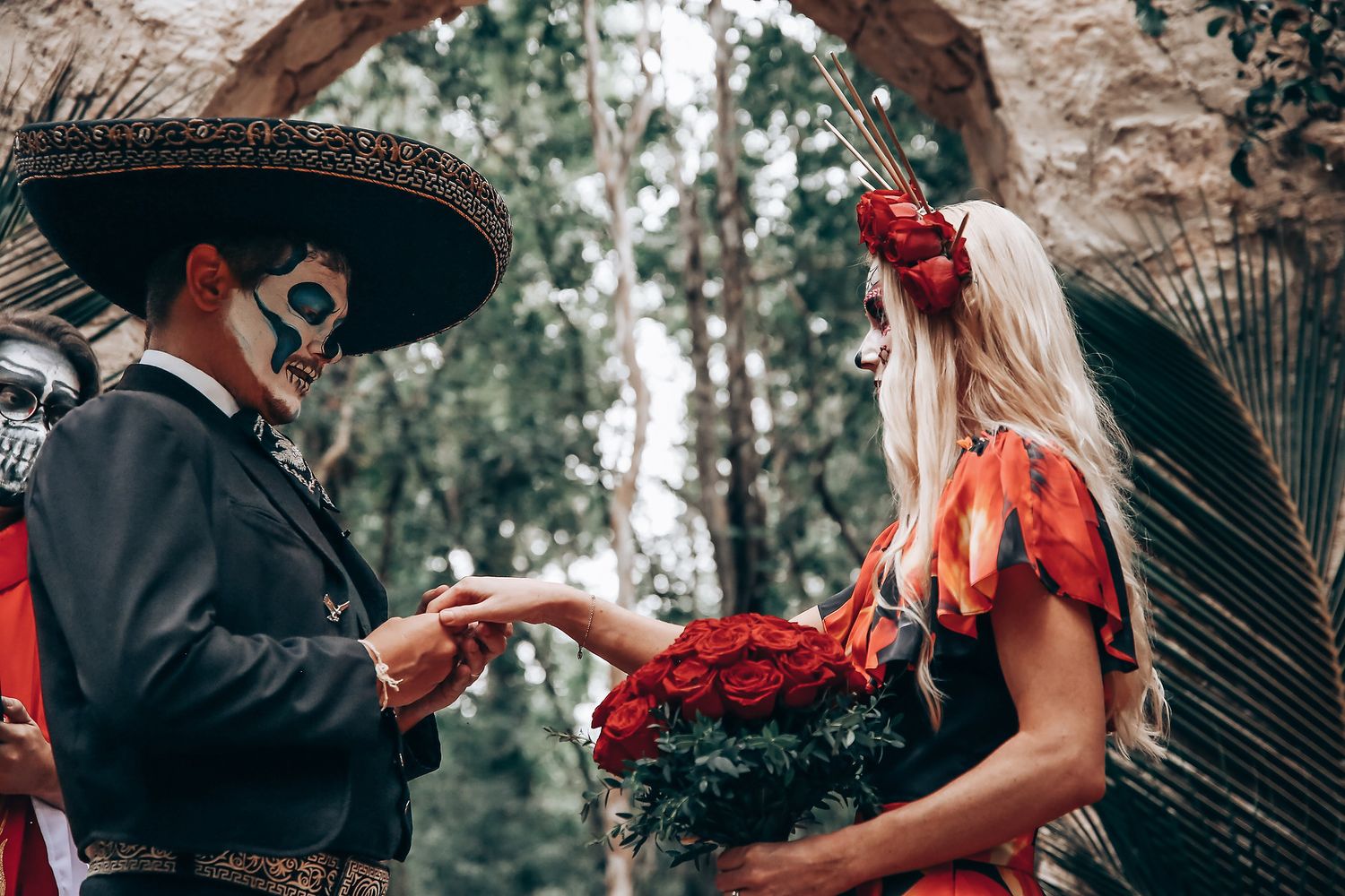 A gothic-themed outdoor photoshoot with figures in black and red attire posed under stone archways.