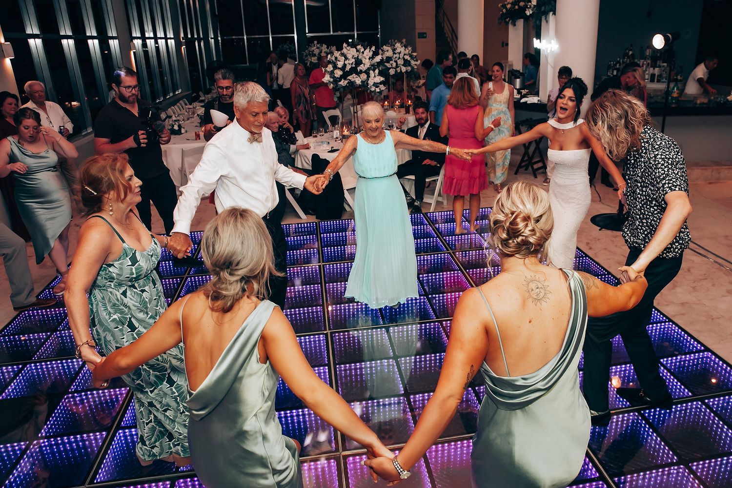 Wedding guests dancing on illuminated LED dance floor with purple lighting at reception.