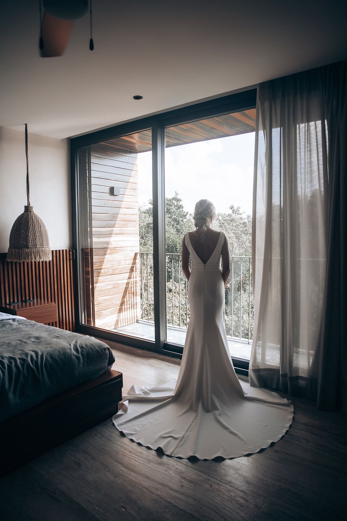 Elegant white wedding dress displayed in a modern room with large windows and natural lighting.