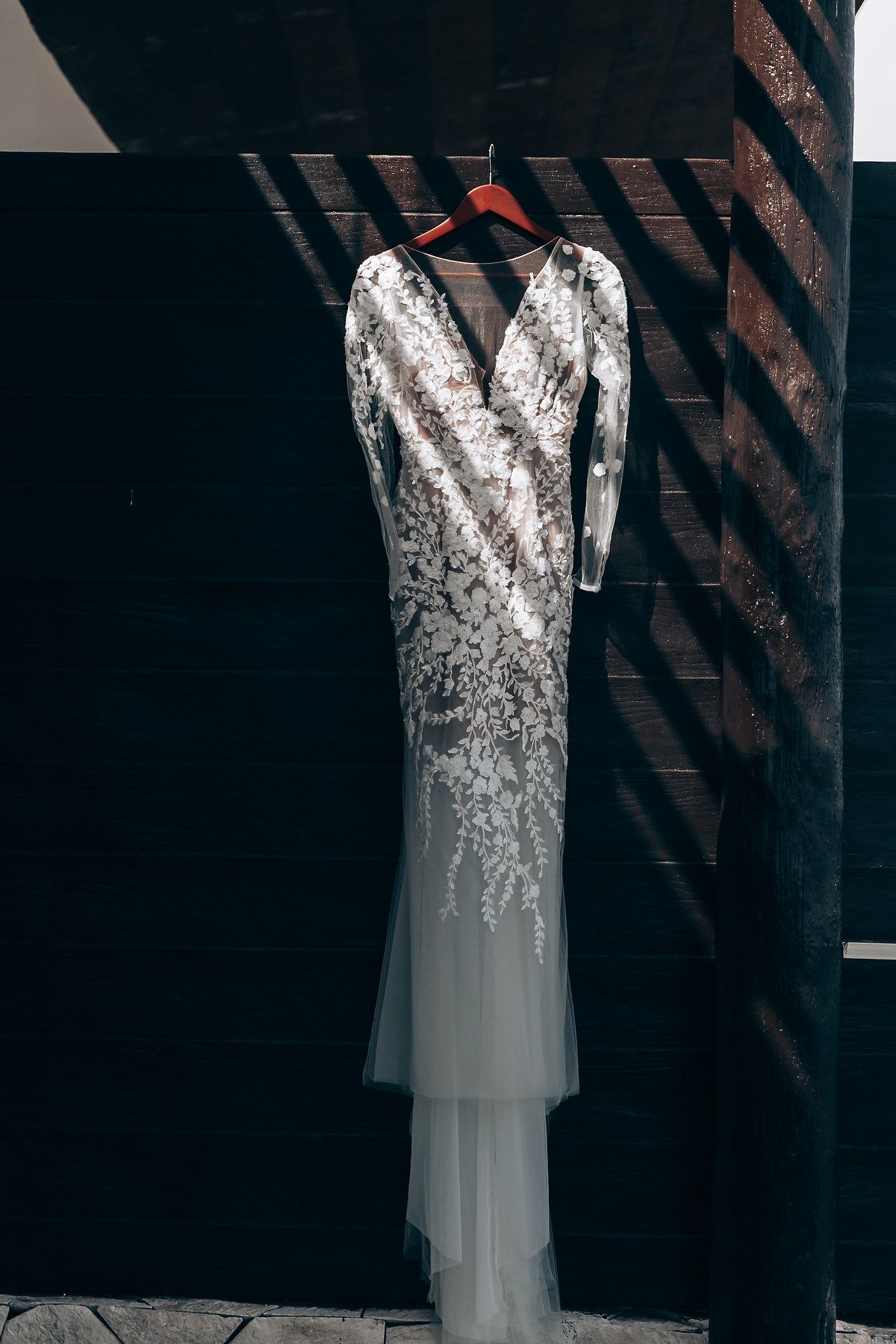Elegant white wedding dress with lace bodice and flowing tulle skirt hanging against dark wooden backdrop.