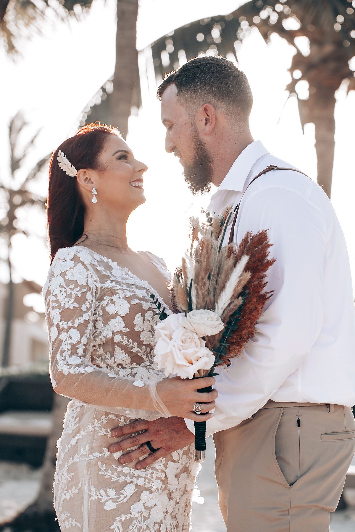 Couple shares intimate first dance moment at sunset beach wedding with dried palm decorations.