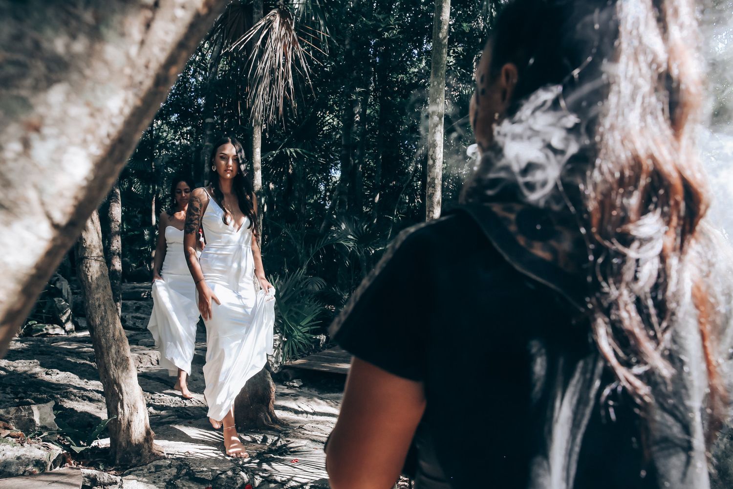 Two people in white dresses walking through a natural wooded setting.