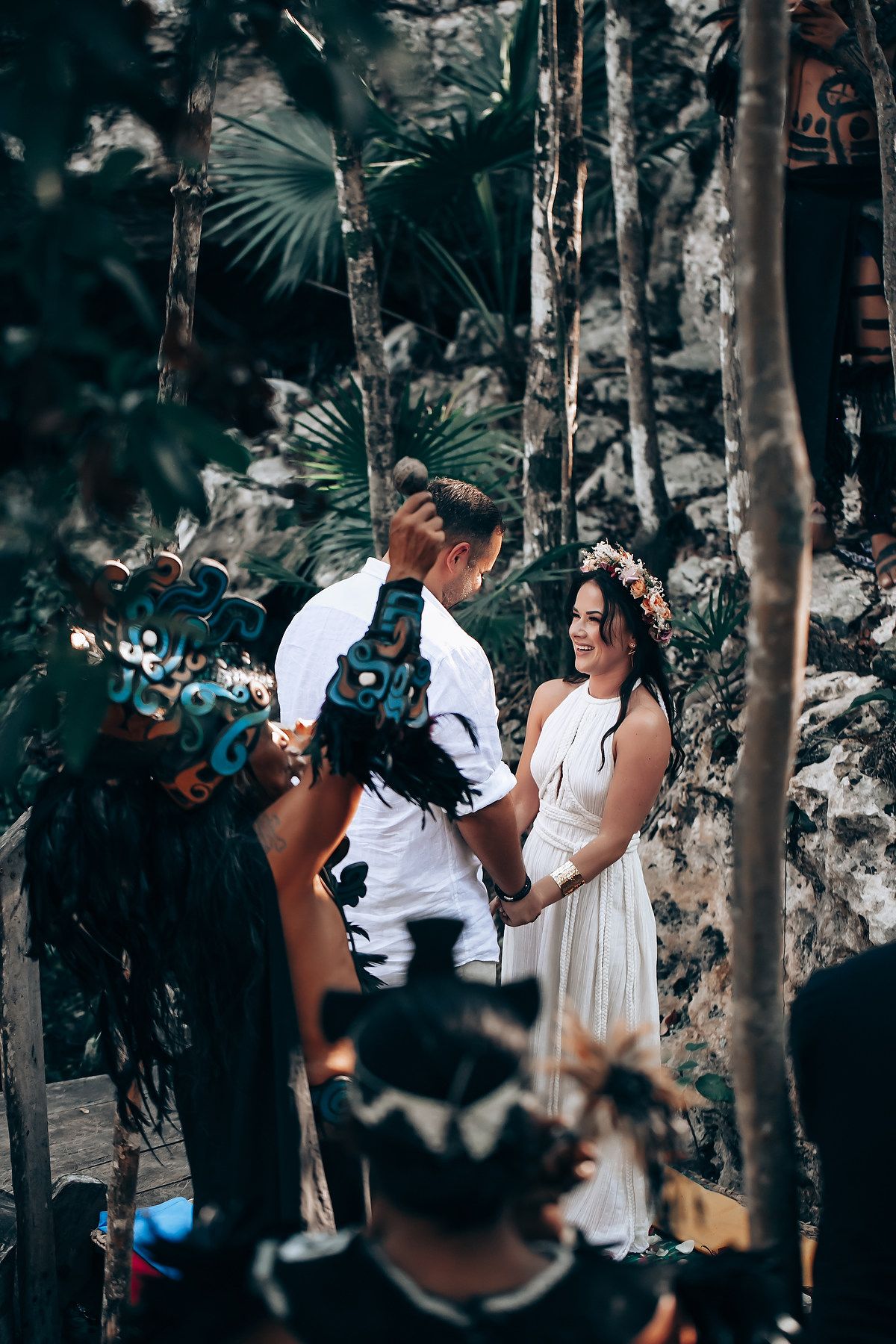 A couple shares an intimate moment together in a lush forest setting with natural lighting filtering through the trees.