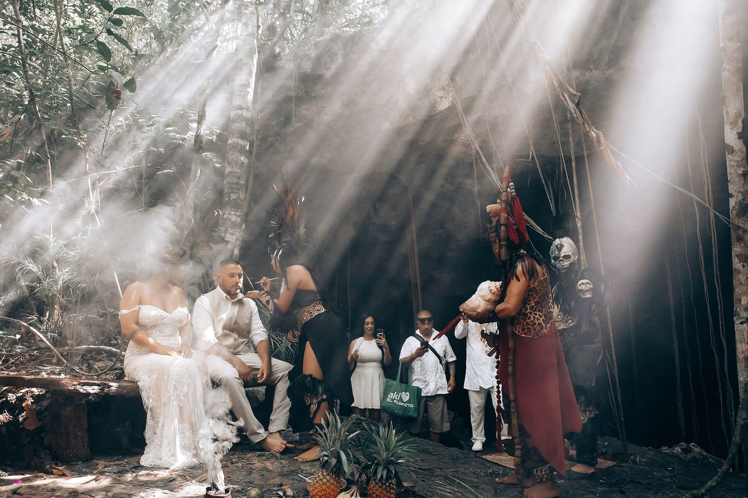 Dramatic rays of sunlight shine through trees onto a gathering of people in a misty forest setting.