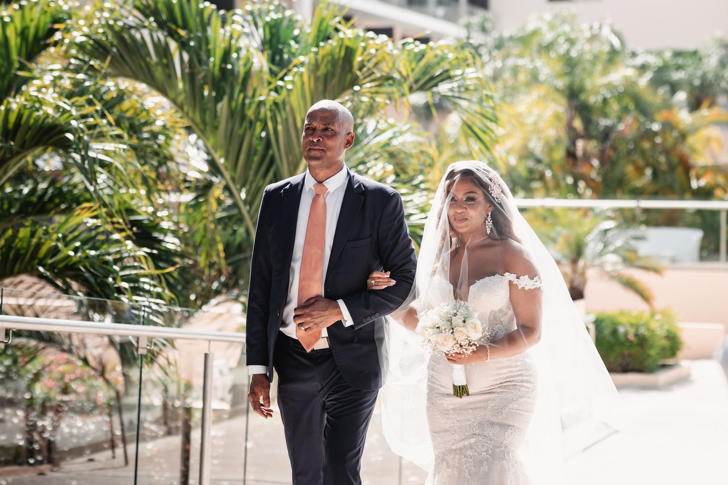Bride in lace wedding dress walks down the aisle with her father at an outdoor wedding.