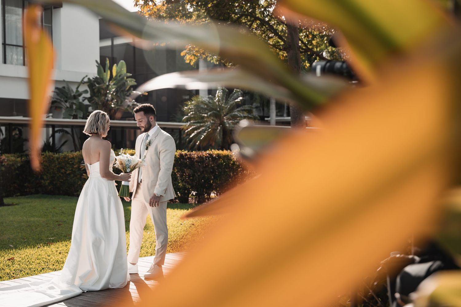 Bride and groom sharing a romantic moment on a sunlit path framed by tropical golden foliage.