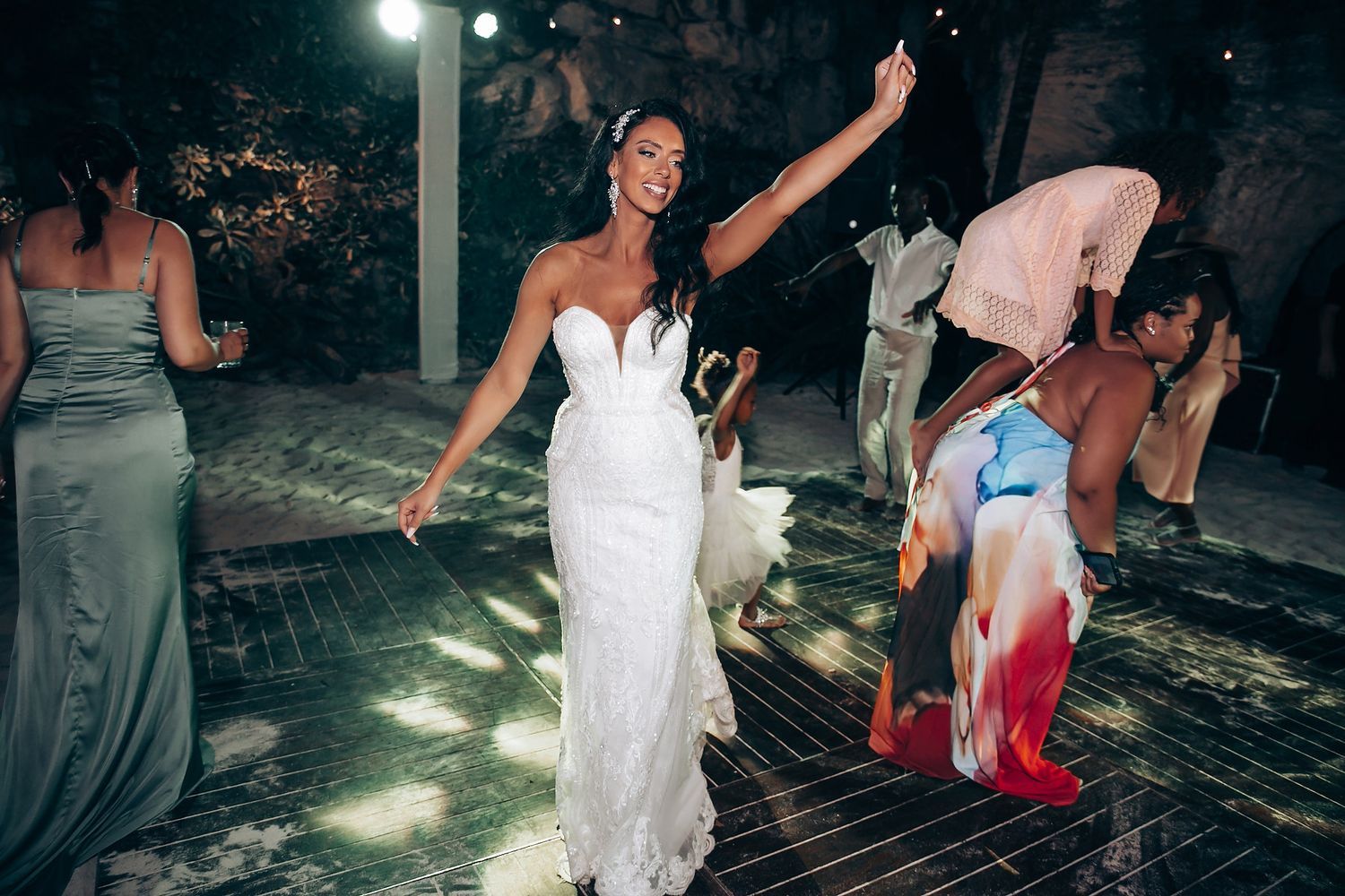 Wedding guests dancing and celebrating on an illuminated dance floor at night.