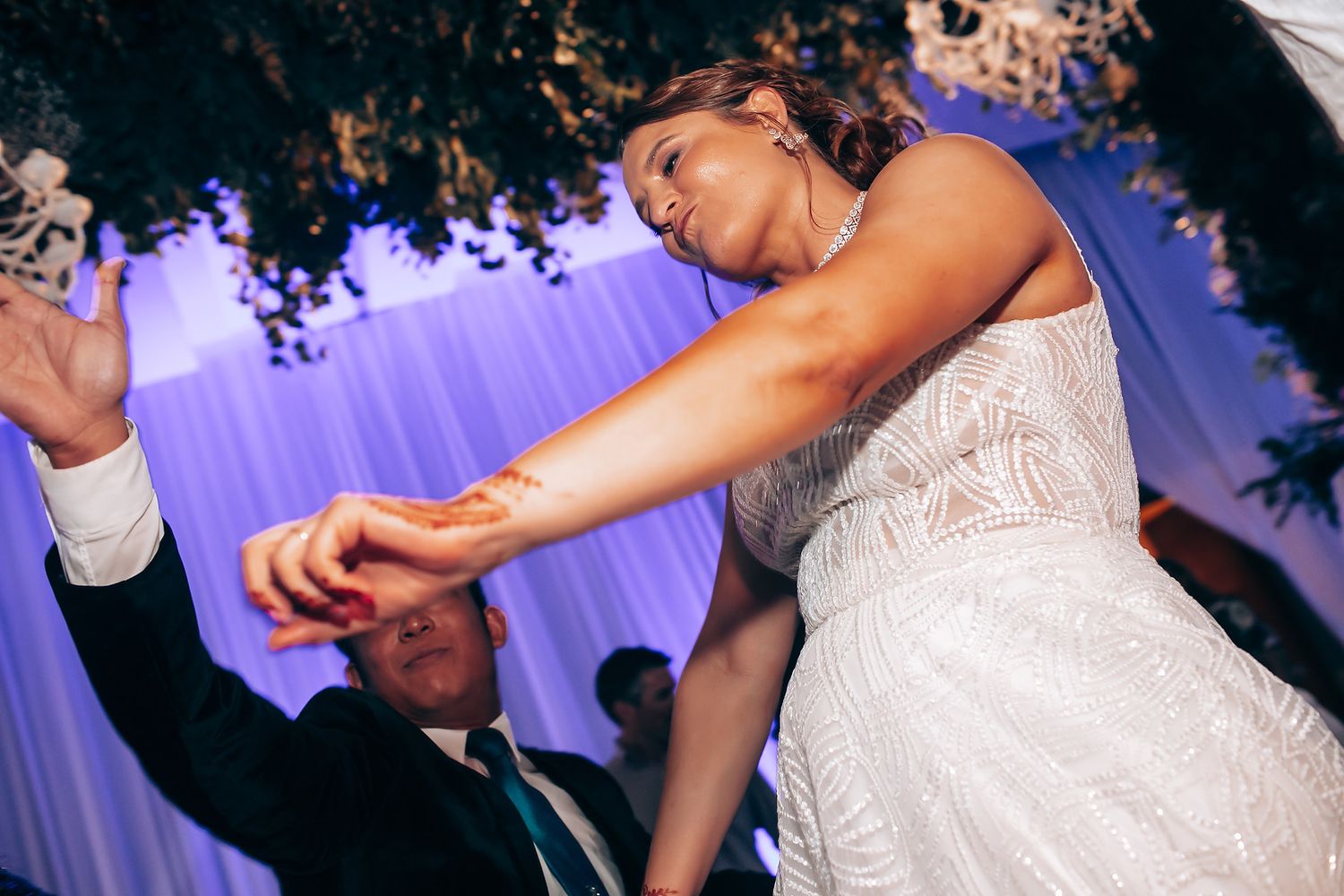 Wedding celebration with guests dancing under purple mood lighting.