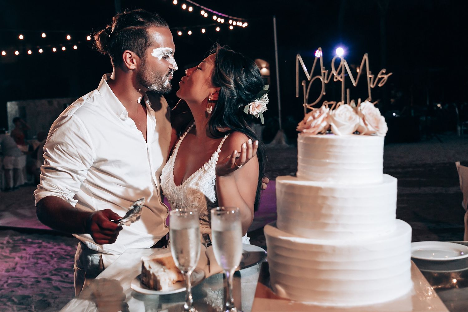 Wedding reception details with string lights and white tiered cake.